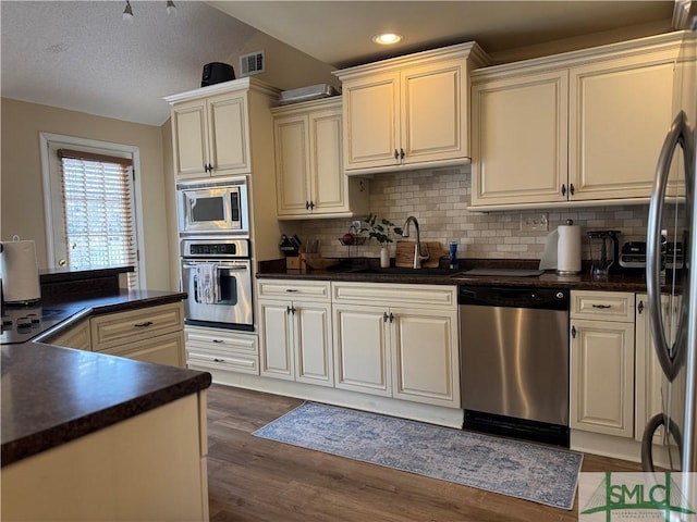 kitchen with visible vents, a sink, stainless steel appliances, vaulted ceiling, and dark countertops