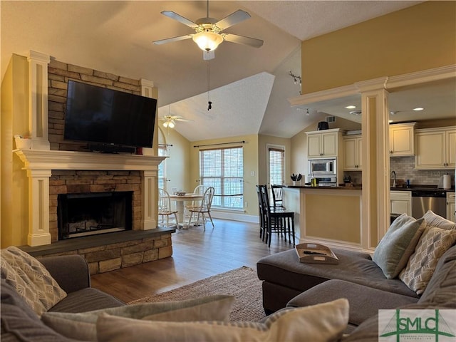 living area featuring a ceiling fan, wood finished floors, a fireplace, and vaulted ceiling