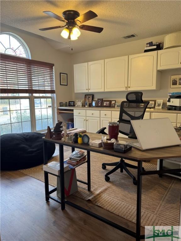 home office with visible vents, a textured ceiling, dark wood-type flooring, and a ceiling fan