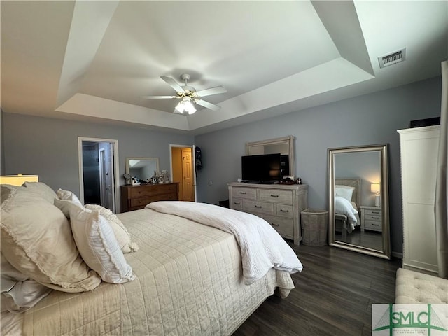 bedroom featuring a tray ceiling, a ceiling fan, visible vents, and dark wood-type flooring