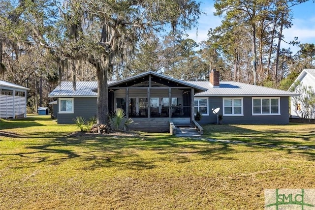 back of house featuring a chimney, metal roof, a yard, and a sunroom