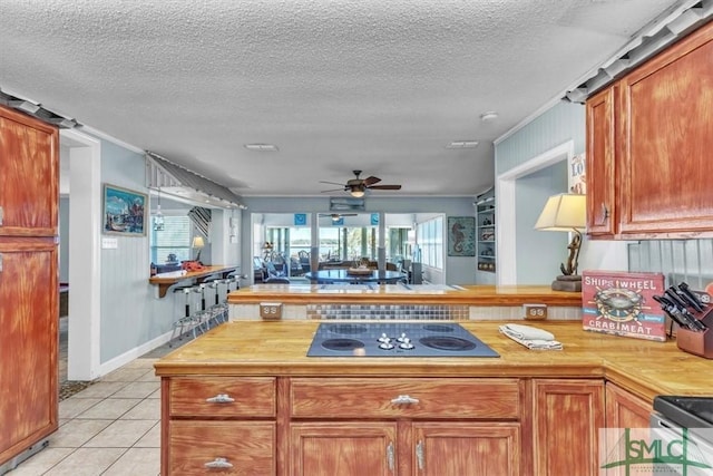 kitchen with open floor plan, a peninsula, light tile patterned floors, black electric stovetop, and ceiling fan