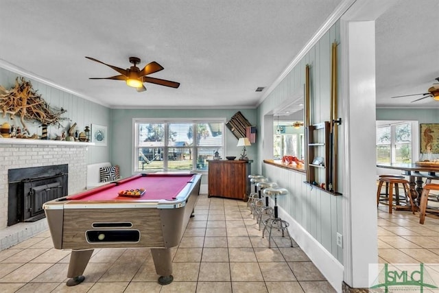 recreation room featuring a fireplace, crown molding, light tile patterned flooring, and a ceiling fan