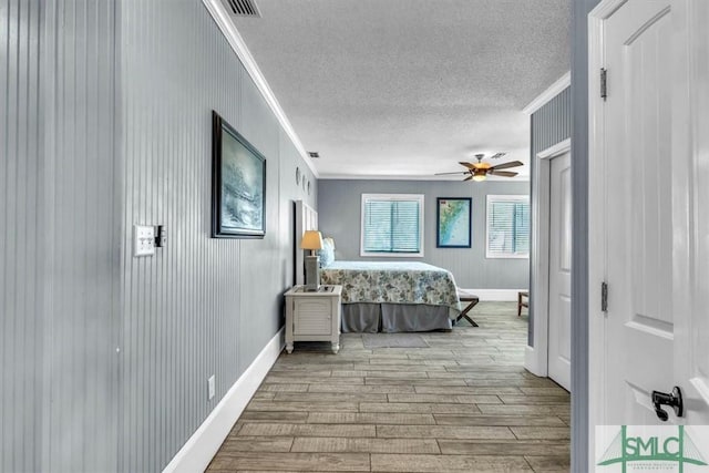 bedroom with a ceiling fan, wood finished floors, baseboards, ornamental molding, and a textured ceiling