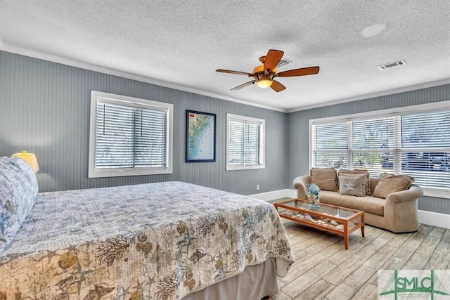 bedroom with wood finished floors, baseboards, visible vents, ceiling fan, and crown molding