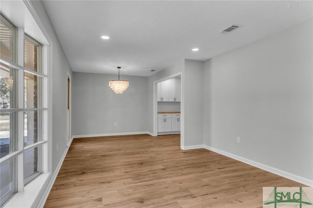 unfurnished dining area with light wood finished floors, visible vents, baseboards, and an inviting chandelier