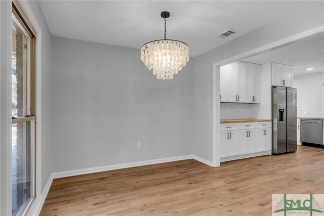 unfurnished dining area featuring a chandelier, visible vents, baseboards, and light wood-style floors