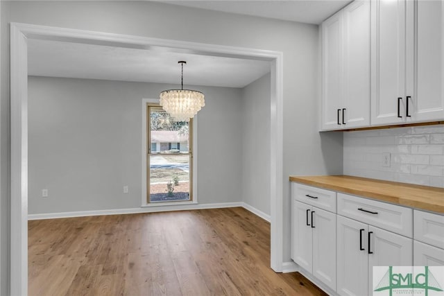 unfurnished dining area with an inviting chandelier, baseboards, and light wood finished floors