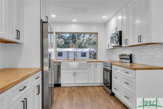 kitchen with a sink, white cabinets, light wood-style floors, appliances with stainless steel finishes, and wood counters