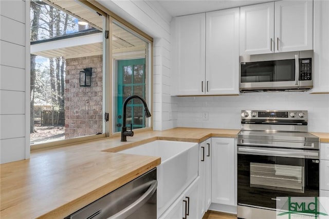 kitchen featuring white cabinetry, butcher block counters, stainless steel appliances, and a sink