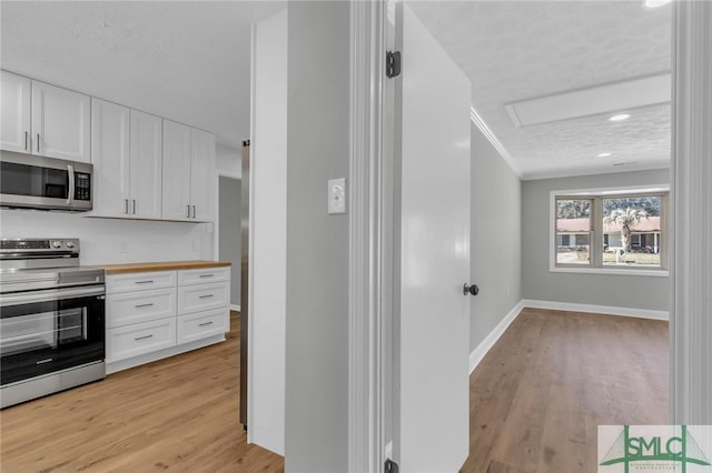 kitchen featuring baseboards, ornamental molding, light wood-style floors, appliances with stainless steel finishes, and white cabinetry