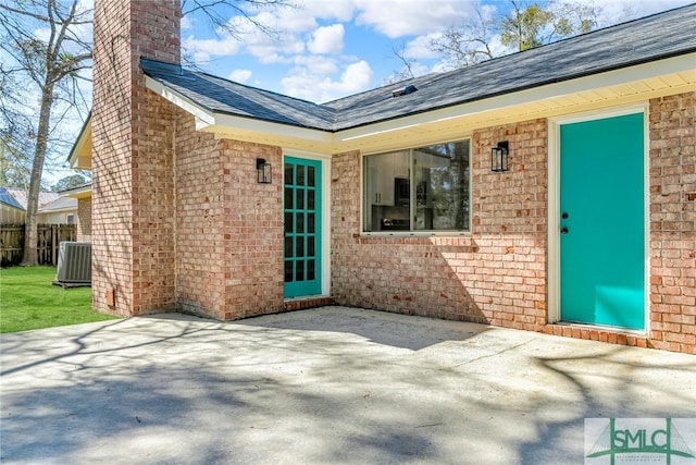 property entrance featuring central AC, fence, brick siding, a chimney, and a patio area