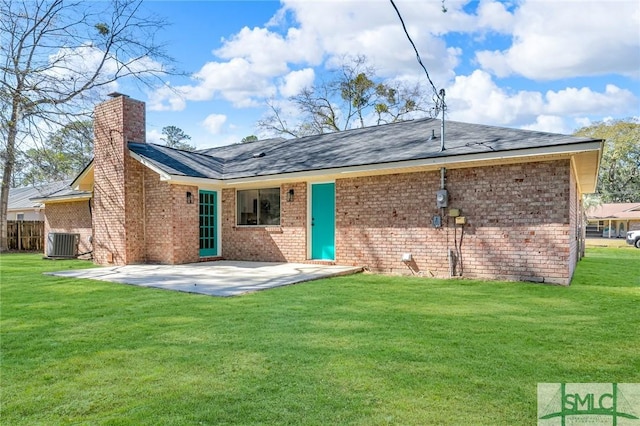 back of house featuring brick siding, a lawn, cooling unit, a chimney, and a patio area