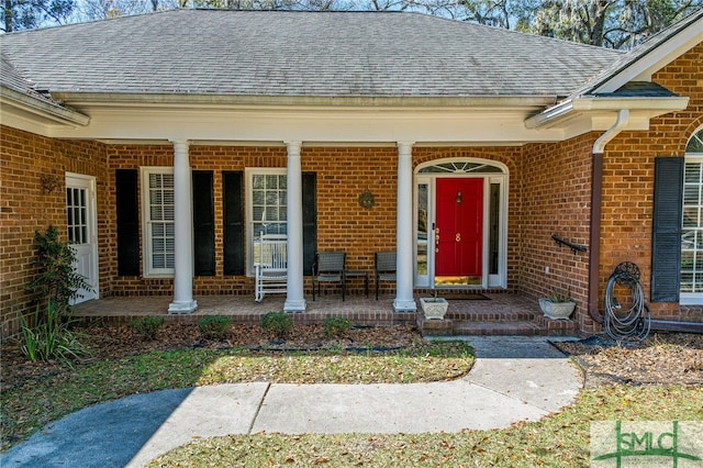 view of exterior entry featuring brick siding, a porch, and roof with shingles