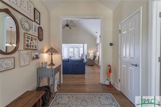 hallway with an inviting chandelier, wood finished floors, baseboards, and high vaulted ceiling