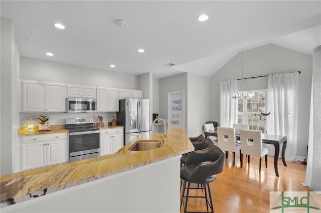 kitchen with light wood-style flooring, a sink, a kitchen breakfast bar, stainless steel appliances, and white cabinets