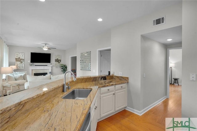 kitchen featuring visible vents, light wood-style flooring, a sink, white cabinets, and a fireplace