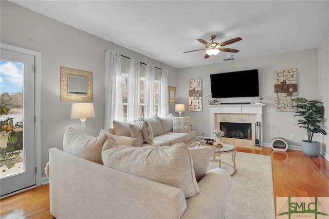 living area featuring visible vents, wood finished floors, a ceiling fan, and a tiled fireplace