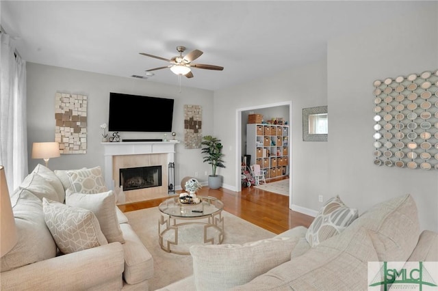 living room with a ceiling fan, wood finished floors, baseboards, and a fireplace