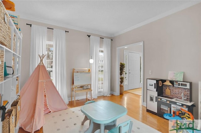 recreation room with baseboards, light wood-style flooring, and ornamental molding