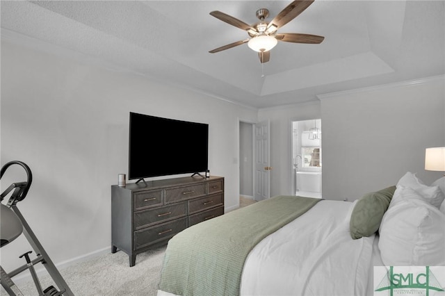 bedroom with baseboards, ceiling fan, light colored carpet, a tray ceiling, and ensuite bath