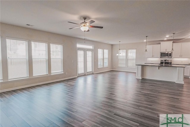 unfurnished living room featuring visible vents, a sink, dark wood-style floors, baseboards, and ceiling fan