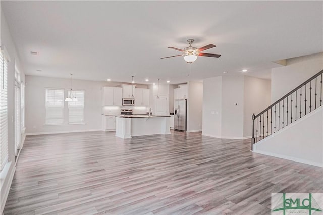 unfurnished living room featuring baseboards, ceiling fan, stairs, and light wood finished floors