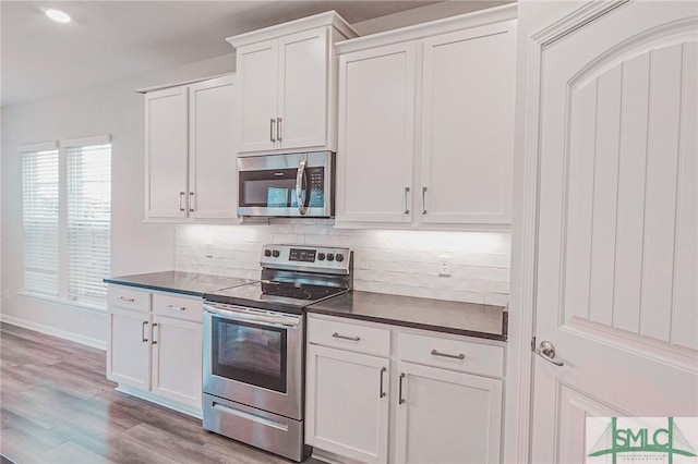 kitchen with stainless steel appliances, white cabinets, dark countertops, tasteful backsplash, and light wood-type flooring