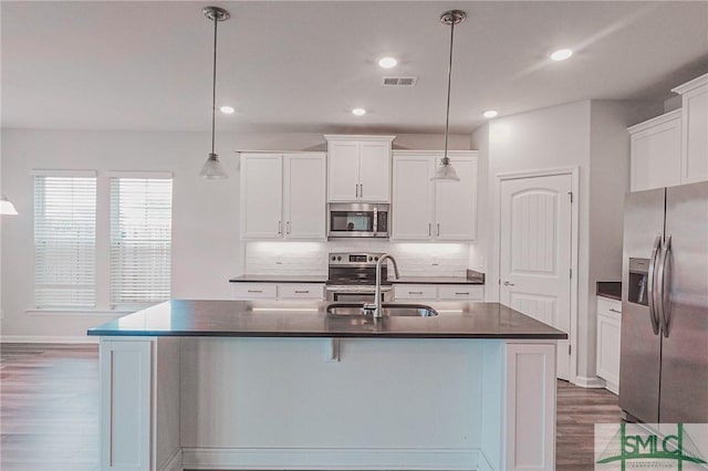 kitchen featuring dark countertops, visible vents, decorative backsplash, stainless steel appliances, and a sink