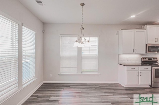 unfurnished dining area featuring visible vents, baseboards, a notable chandelier, and wood finished floors