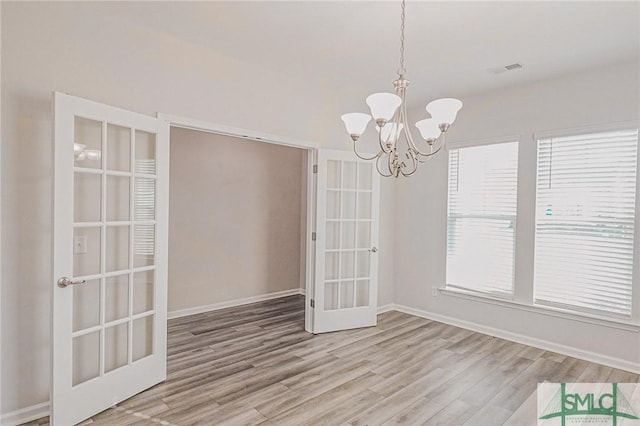 unfurnished dining area with a chandelier, plenty of natural light, baseboards, and wood finished floors