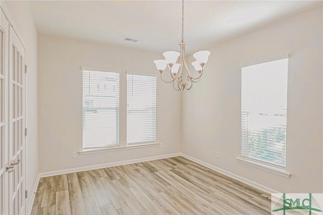 empty room featuring light wood-type flooring, baseboards, a notable chandelier, and visible vents