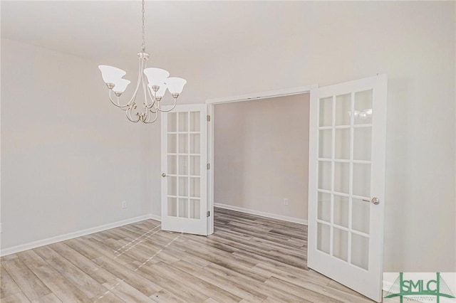 empty room featuring a chandelier, french doors, baseboards, and wood finished floors