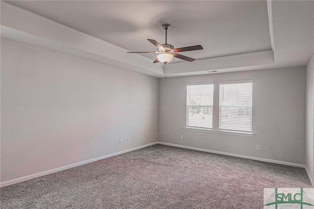 carpeted empty room featuring a ceiling fan, a raised ceiling, and baseboards