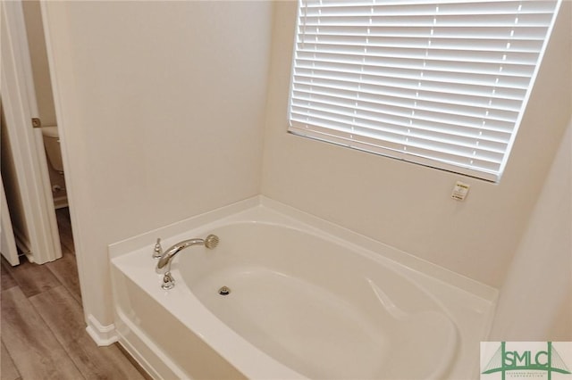 bathroom featuring a garden tub, wood finished floors, and toilet