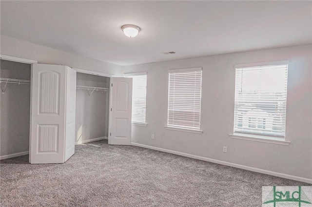 unfurnished bedroom featuring visible vents, baseboards, two closets, and carpet flooring