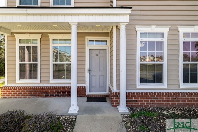 doorway to property with a porch and brick siding