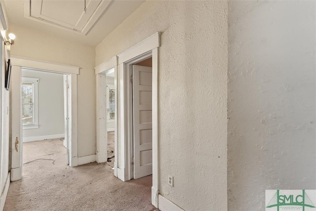 corridor featuring a textured wall, baseboards, and light carpet