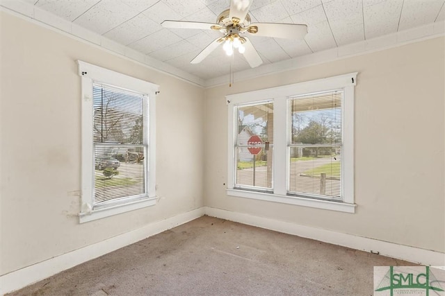 empty room featuring a wealth of natural light, a ceiling fan, carpet, and ornamental molding