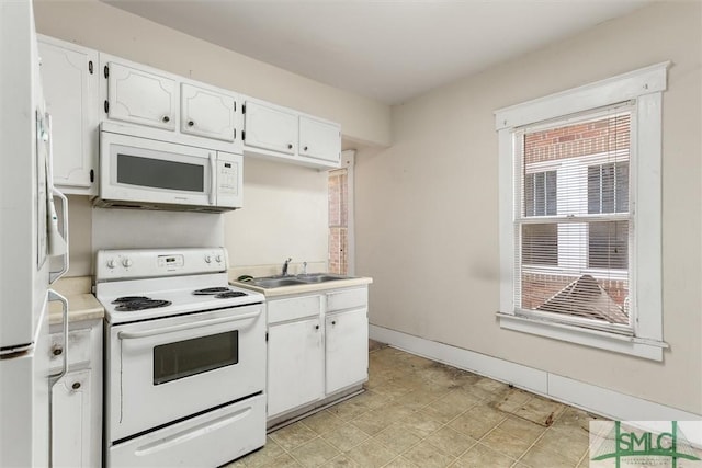 kitchen with baseboards, light countertops, white cabinets, white appliances, and a sink