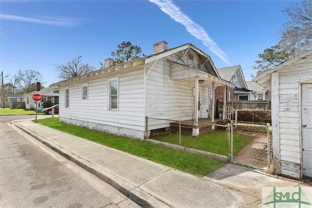 view of property exterior with a gate, a chimney, a yard, and fence