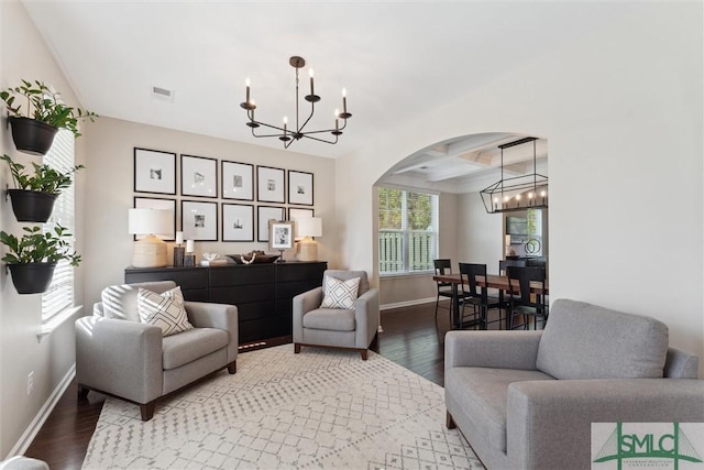 living room with wood finished floors, arched walkways, coffered ceiling, and a chandelier