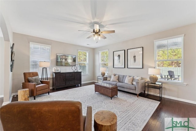 living area with dark wood-style floors, arched walkways, a ceiling fan, and baseboards