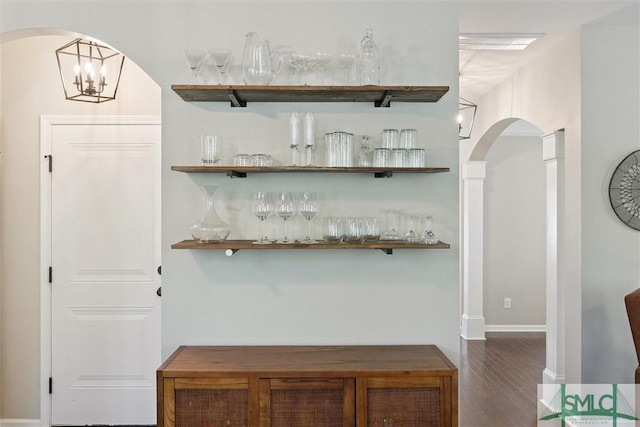 bar featuring arched walkways, a bar, baseboards, and wood finished floors