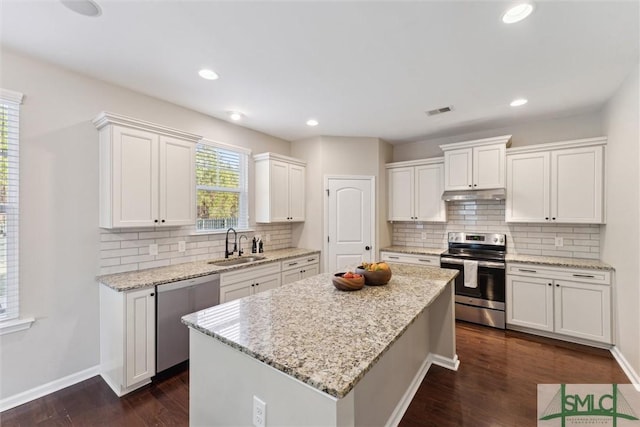 kitchen with dark wood-style flooring, white cabinets, under cabinet range hood, appliances with stainless steel finishes, and a center island