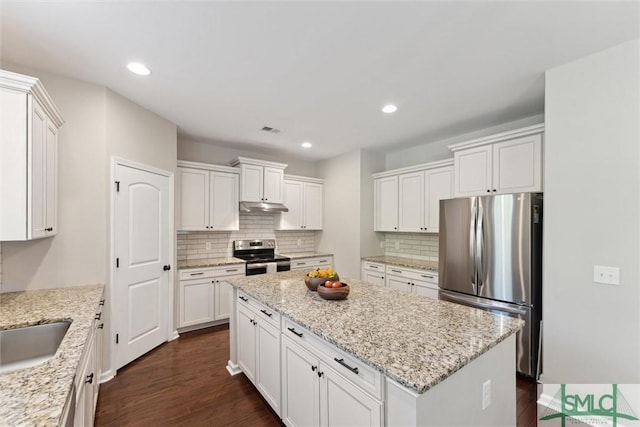 kitchen with under cabinet range hood, appliances with stainless steel finishes, dark wood finished floors, and a center island