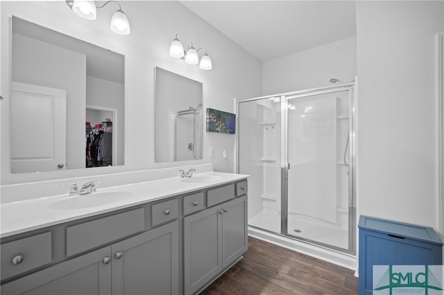 bathroom featuring double vanity, wood finished floors, a stall shower, and a sink