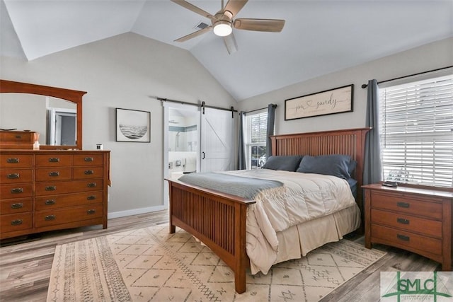 bedroom with a ceiling fan, baseboards, vaulted ceiling, a barn door, and light wood-type flooring