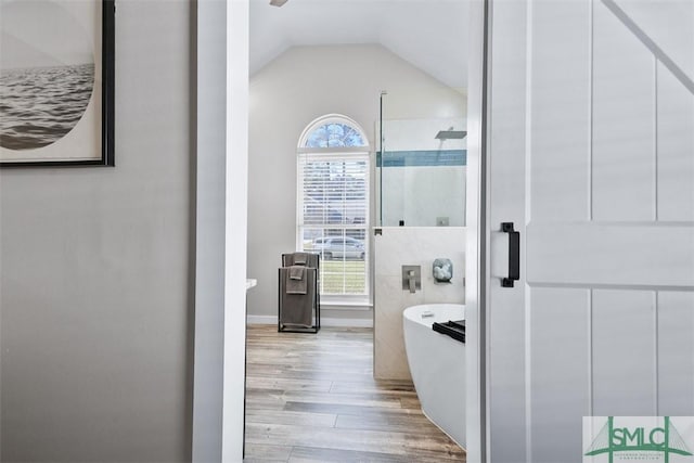 bathroom with a shower stall, a freestanding tub, wood finished floors, and vaulted ceiling