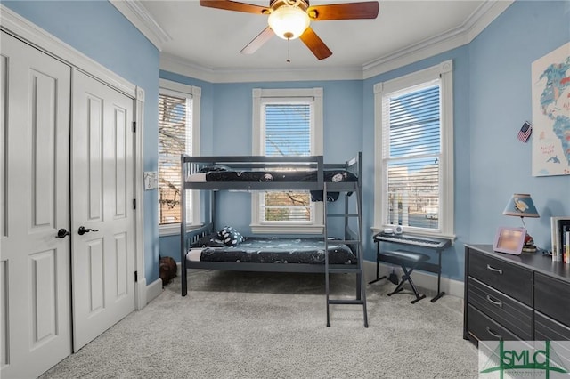 carpeted bedroom with crown molding, a ceiling fan, baseboards, and a closet